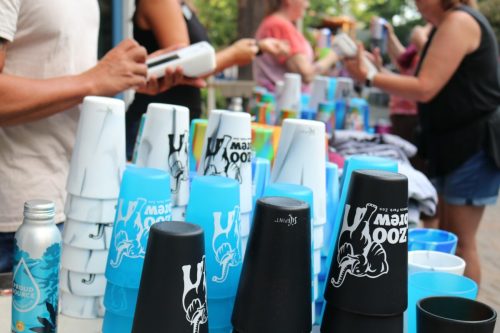 A table filled with colorful cups and merchandise, with people interacting in the background.