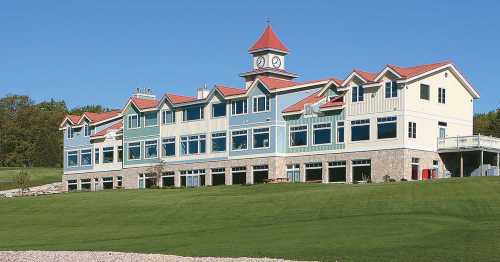 A large, modern building with a clock tower, surrounded by green grass and clear blue skies.