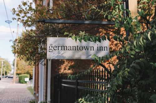 Sign for "the germantown inn" surrounded by greenery, with a brick building in the background.