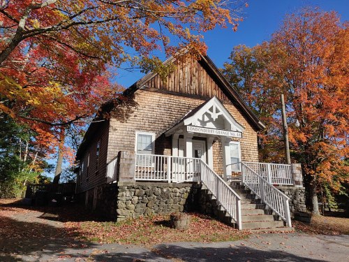 A charming wooden building with a steep roof, surrounded by vibrant autumn foliage and a clear blue sky.