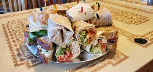 A platter of assorted sandwiches and wraps, garnished with colorful picks, arranged on a decorative table.