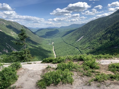 A scenic view of a lush green valley surrounded by mountains under a partly cloudy sky.