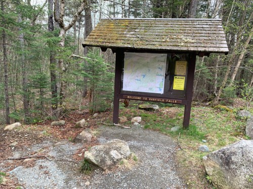 A wooden information kiosk in a forest, featuring a map and a welcome sign for Garfield Falls.