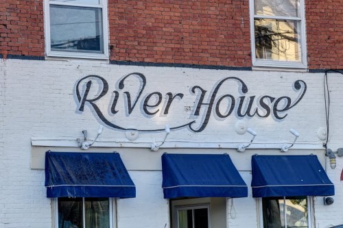 Sign for "River House" on a brick building with blue awnings below.