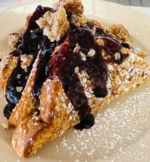 A plate of French toast topped with blueberry sauce, granola, and powdered sugar.