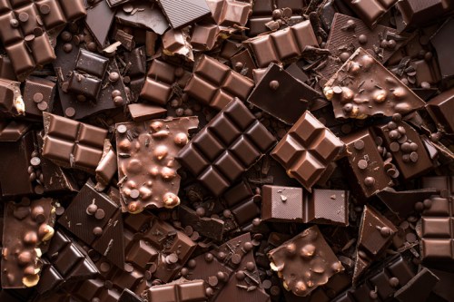 A variety of dark chocolate bars and pieces scattered on a surface, including chocolate chips and nut-covered bars.