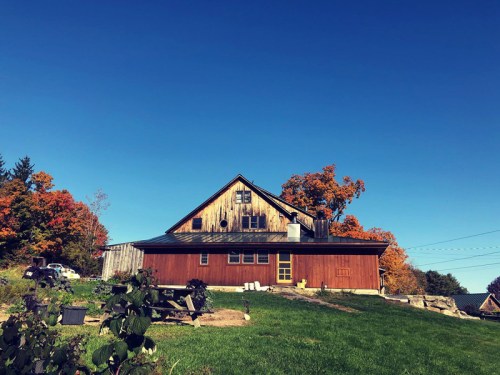 A rustic barn with a wooden exterior, surrounded by vibrant autumn trees under a clear blue sky.