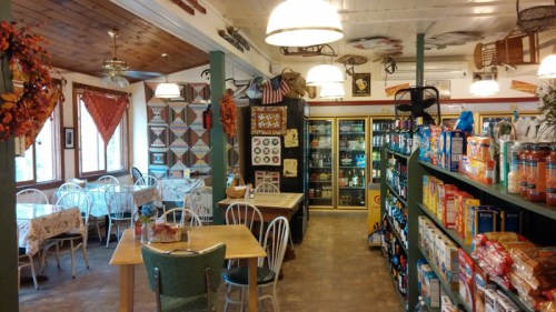 Cozy diner interior with wooden tables, chairs, and shelves stocked with groceries, decorated with rustic accents.