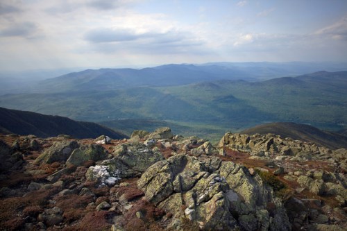 A panoramic view of rolling green mountains and rocky terrain under a cloudy sky.