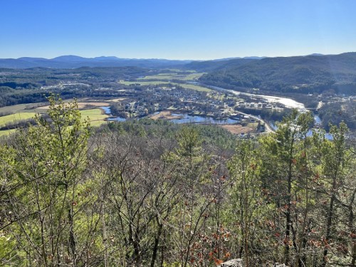A panoramic view of a valley with a river, fields, and distant mountains under a clear blue sky.