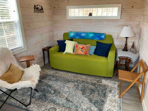 Cozy living space featuring a green sofa with colorful pillows, a white lamp, and a textured rug.