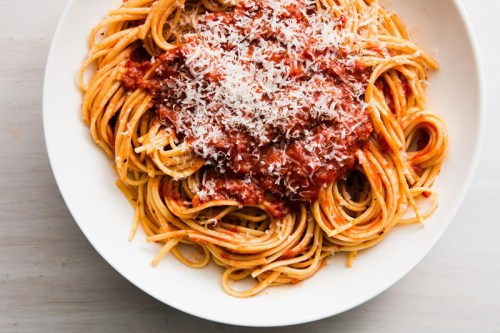 A plate of spaghetti topped with marinara sauce and grated cheese, served on a white dish.