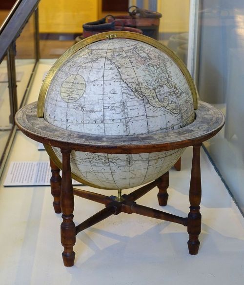 A vintage globe on a wooden stand, displaying detailed maps of the world, set in a museum display.