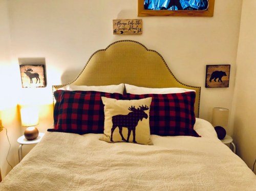 Cozy bedroom with a plaid-patterned pillow, a light-colored quilt, and rustic wall art featuring wildlife.