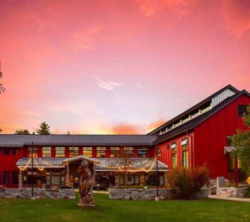 A red building with large windows and a stone patio, set against a colorful sunset sky.
