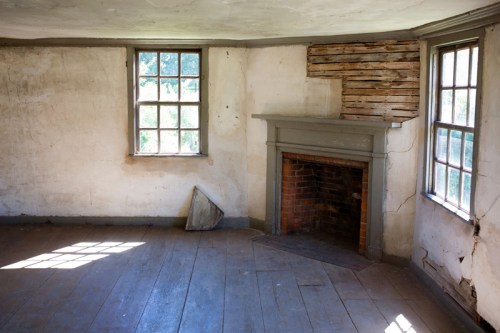 Interior of a rustic room with two windows, a brick fireplace, and weathered walls, featuring wooden floorboards.