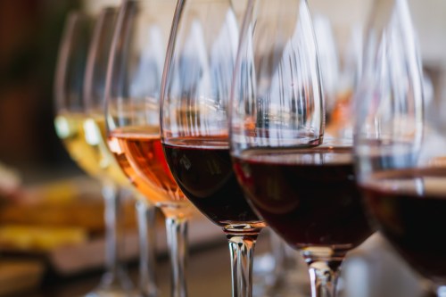 A row of wine glasses filled with white, rosé, and red wines, reflecting light in a warm setting.