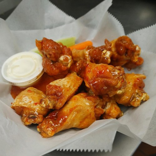 A plate of spicy chicken wings with a side of ranch dressing and celery sticks.