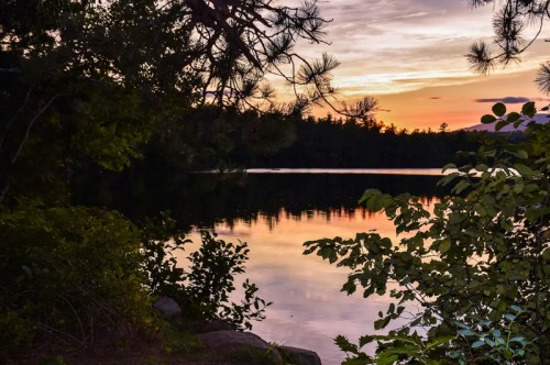 A serene lake at sunset, surrounded by trees and reflecting colorful skies.