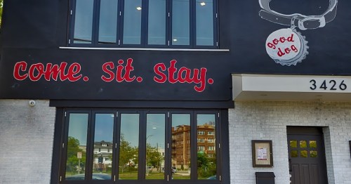 Exterior of a building with large windows and a sign that reads "come. sit. stay." and "good dog." at 3426.