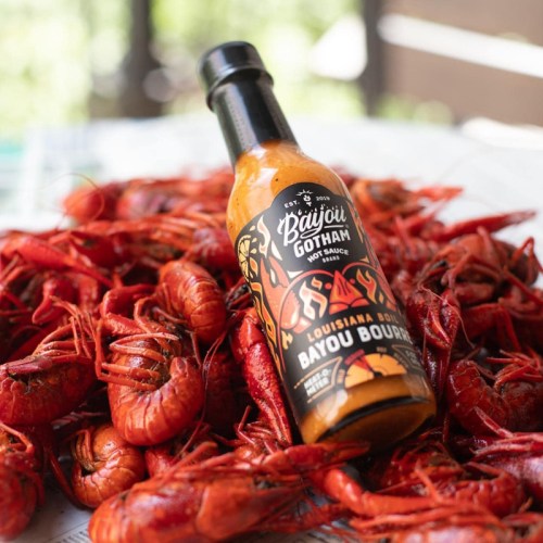 A bottle of Bayou Gotham hot sauce sits atop a pile of bright red crawfish.