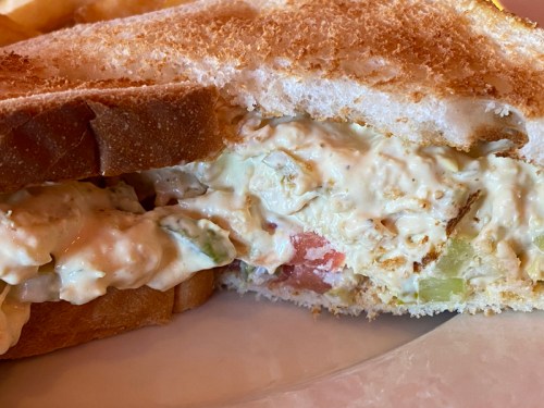 Close-up of a toasted sandwich filled with creamy chicken salad, including diced vegetables and herbs.