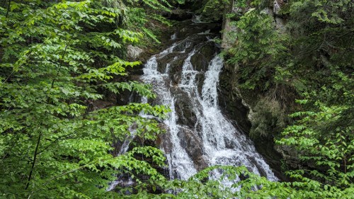 A serene waterfall cascading down rocky terrain, surrounded by lush green foliage.