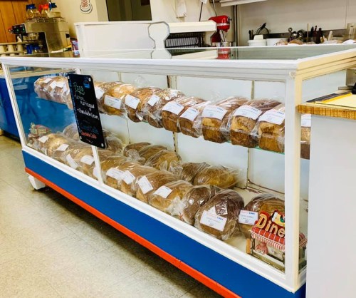 A display case filled with various types of bread, neatly packaged and labeled, in a bakery setting.
