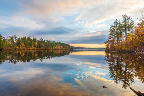 A serene lake at sunset, reflecting trees and colorful clouds in calm waters.