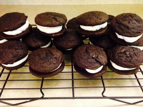 A tray of chocolate whoopie pies filled with white cream, arranged neatly on a cooling rack.