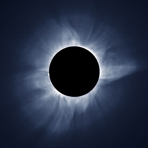 A total solar eclipse with a darkened sun surrounded by a glowing corona and wispy solar flares.