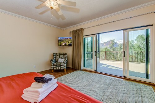 A cozy bedroom with a red bedspread, a TV, and sliding glass doors leading to a balcony with scenic views.