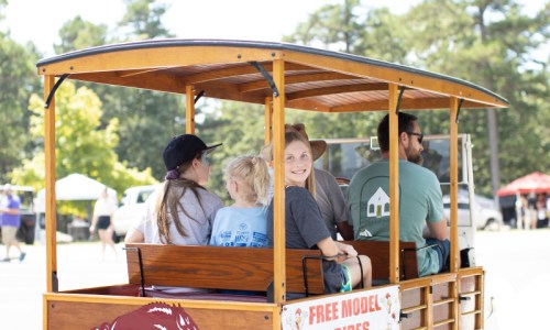 A group of people, including a child, enjoying a ride on a wooden cart at an outdoor event.