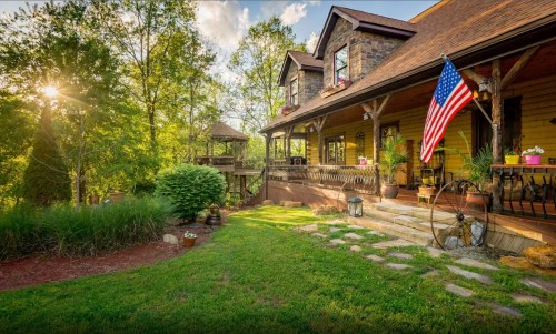 A charming house with a porch, American flag, and lush greenery, bathed in warm sunlight.