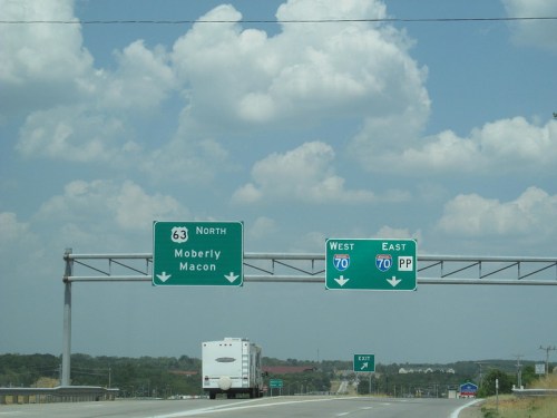 Highway sign indicating directions to Moberly and Macon, with exits for I-70 West and East under a cloudy sky.