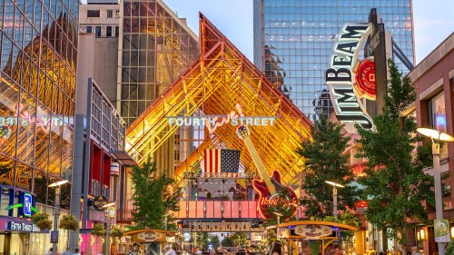 Vibrant urban scene featuring a large, colorful structure with an American flag, surrounded by shops and greenery.
