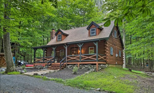 A charming log cabin surrounded by lush green trees, featuring a porch and stone pathway.
