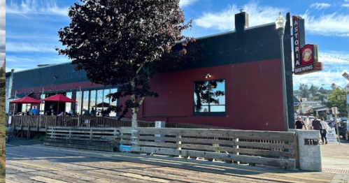 Exterior of Astoria Brewing with a red and black facade, outdoor seating, and a clear blue sky.