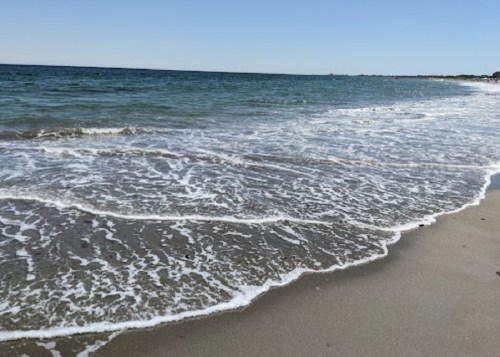 Waves gently lapping at a sandy beach under a clear blue sky.