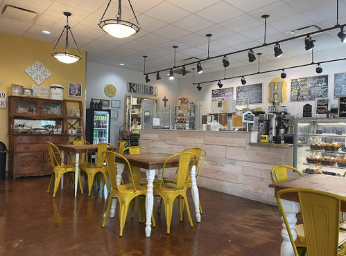 Cozy café interior with yellow chairs, wooden tables, and a counter displaying baked goods and coffee.