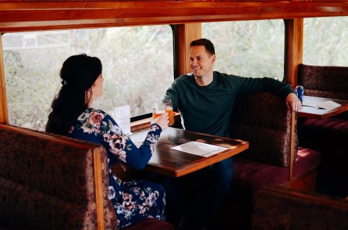 A couple sits at a cozy table in a train car, enjoying drinks and smiling at each other.