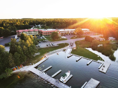 Aerial view of a lakeside resort at sunset, featuring docks, boats, and lush green surroundings.