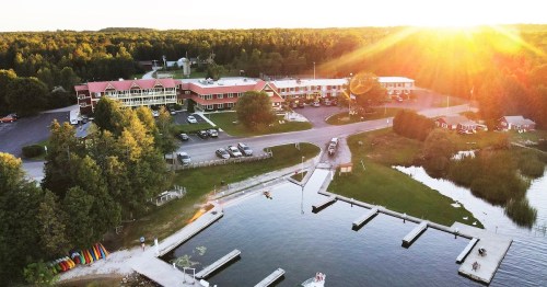Aerial view of a lakeside resort with parking, docks, and colorful kayaks, surrounded by trees and a sunset glow.