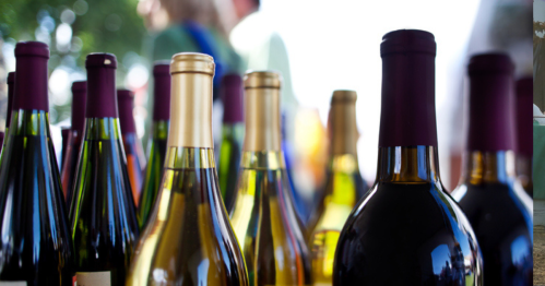 A close-up of various wine bottles with colorful labels and caps, set against a blurred outdoor background.