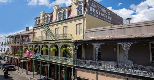Historic buildings with balconies and greenery, featuring Antoine's Restaurant sign, in a vibrant street scene.