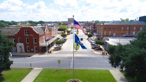 Aerial view of a town square with an American flag and a South Carolina flag, surrounded by historic buildings and trees.