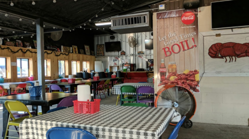 Interior of a casual restaurant with colorful chairs, checkered tables, and a large sign promoting seafood boils.