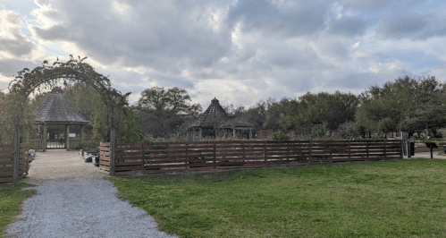 A pathway leads to a park with wooden fences, pavilions, and cloudy skies in the background.