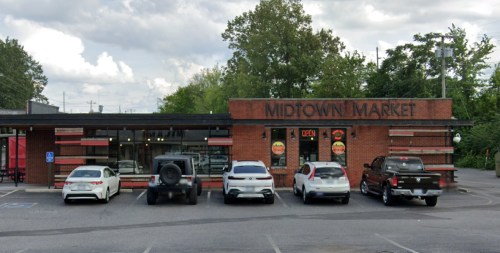 A brick building with "Midtown Market" signage, featuring several parked cars in front and trees in the background.