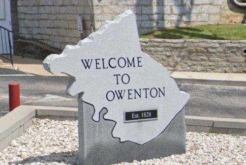 Welcome sign for Owenton, Kentucky, shaped like the state, established in 1828, with a stone texture.